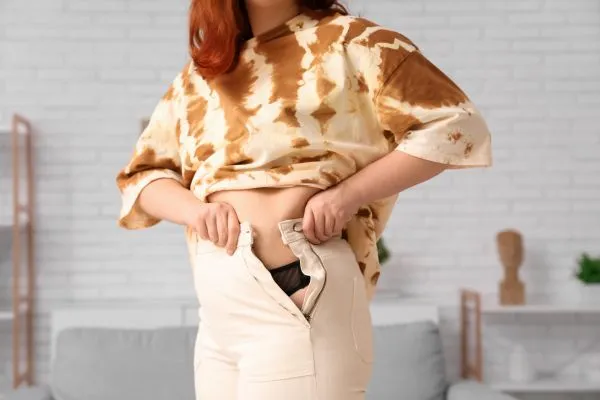 Image of woman trying to do her trousers up after pregnancy weight gain Frimley