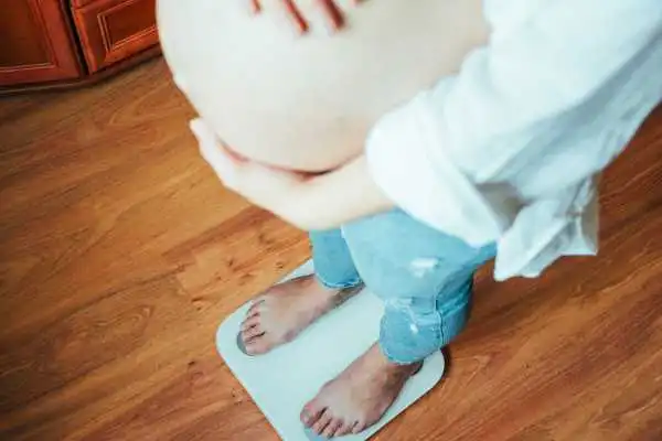 Image of woman weighing herself and experiencing weight gain through pregnancy Frimley